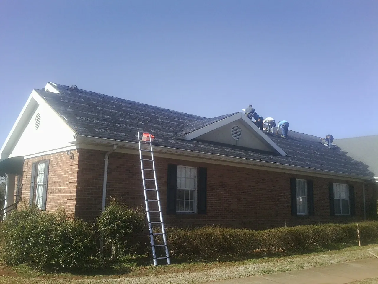 Crew tearing shingles off a brick ranch roof with a ladder set — Metal Roof Repair work by our crew in Platteville