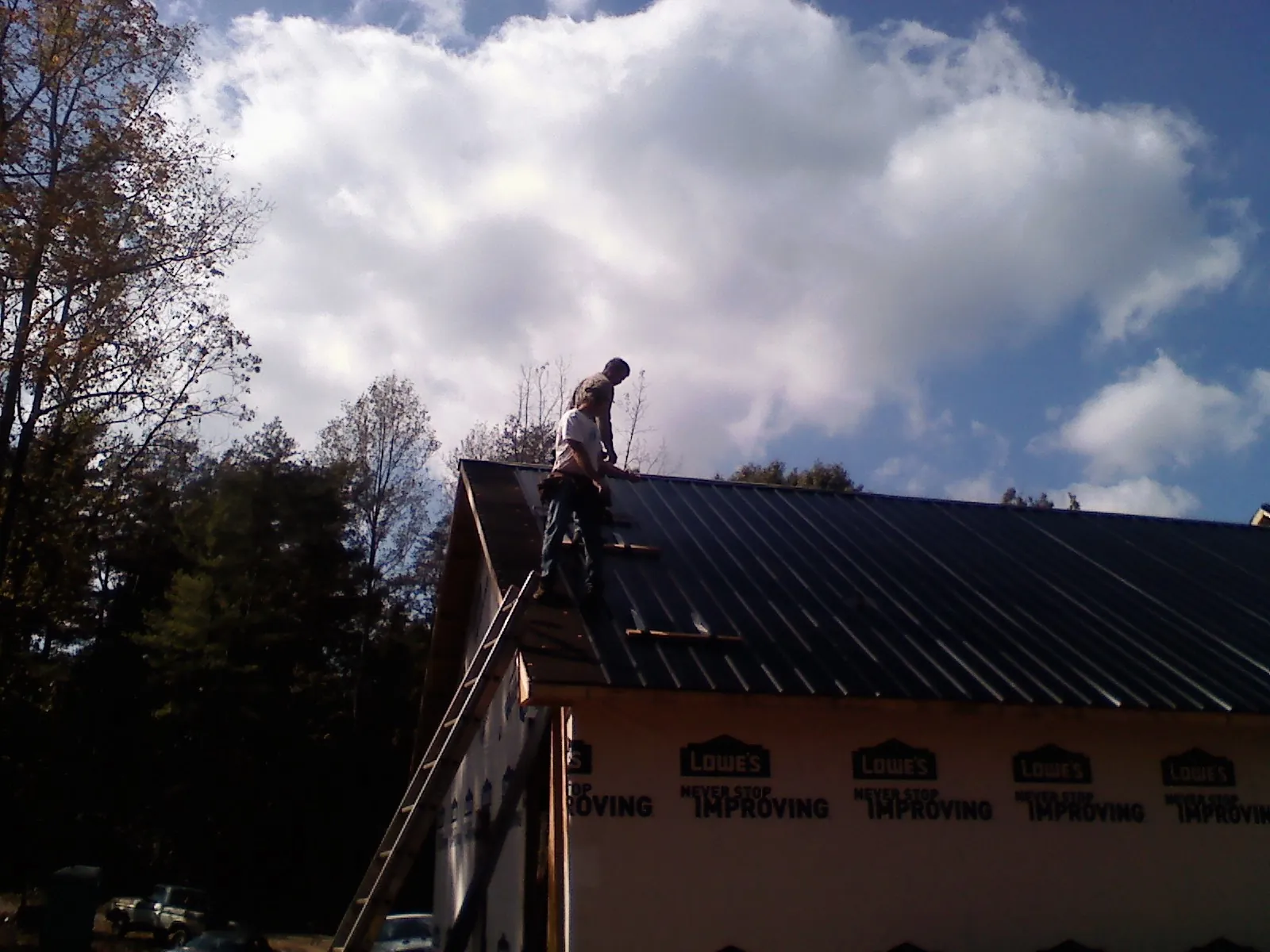 Roofer fastening dark metal panels high against a cloudy sky, from a Roof Inspection job in Platteville